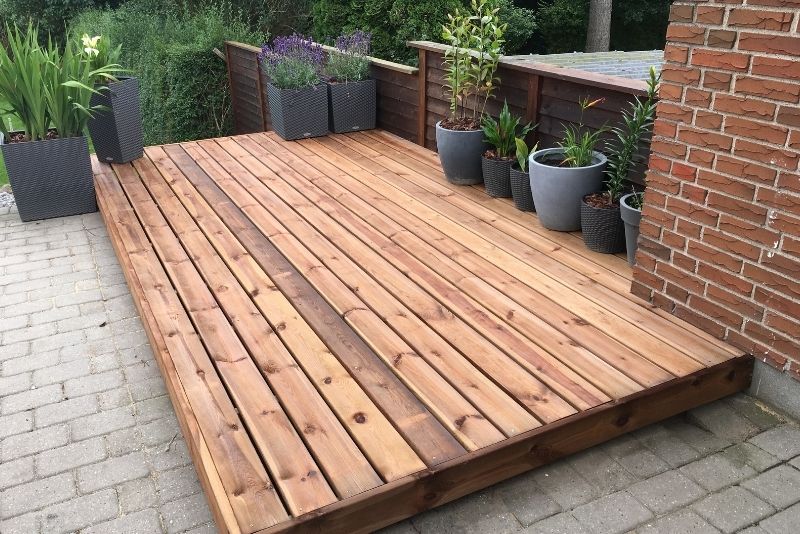 Ground-level timber deck with potted plants against a brick courtyard wall