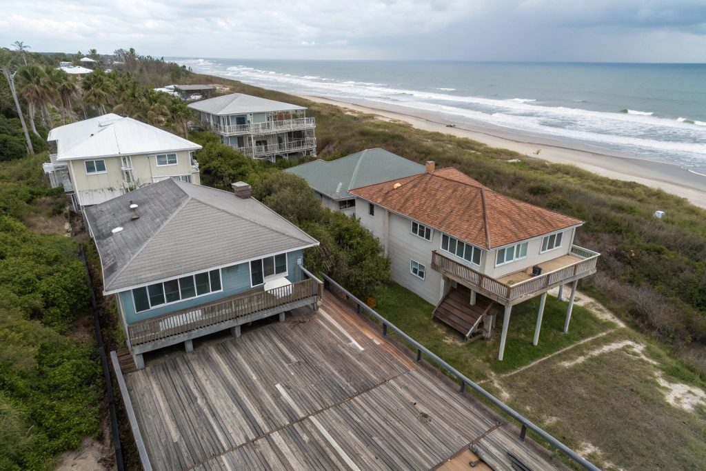 Aerial view of three neighboring Burleigh Heads beachfront properties with different decking materials showing visible condition differences after 10 years of salt exposure